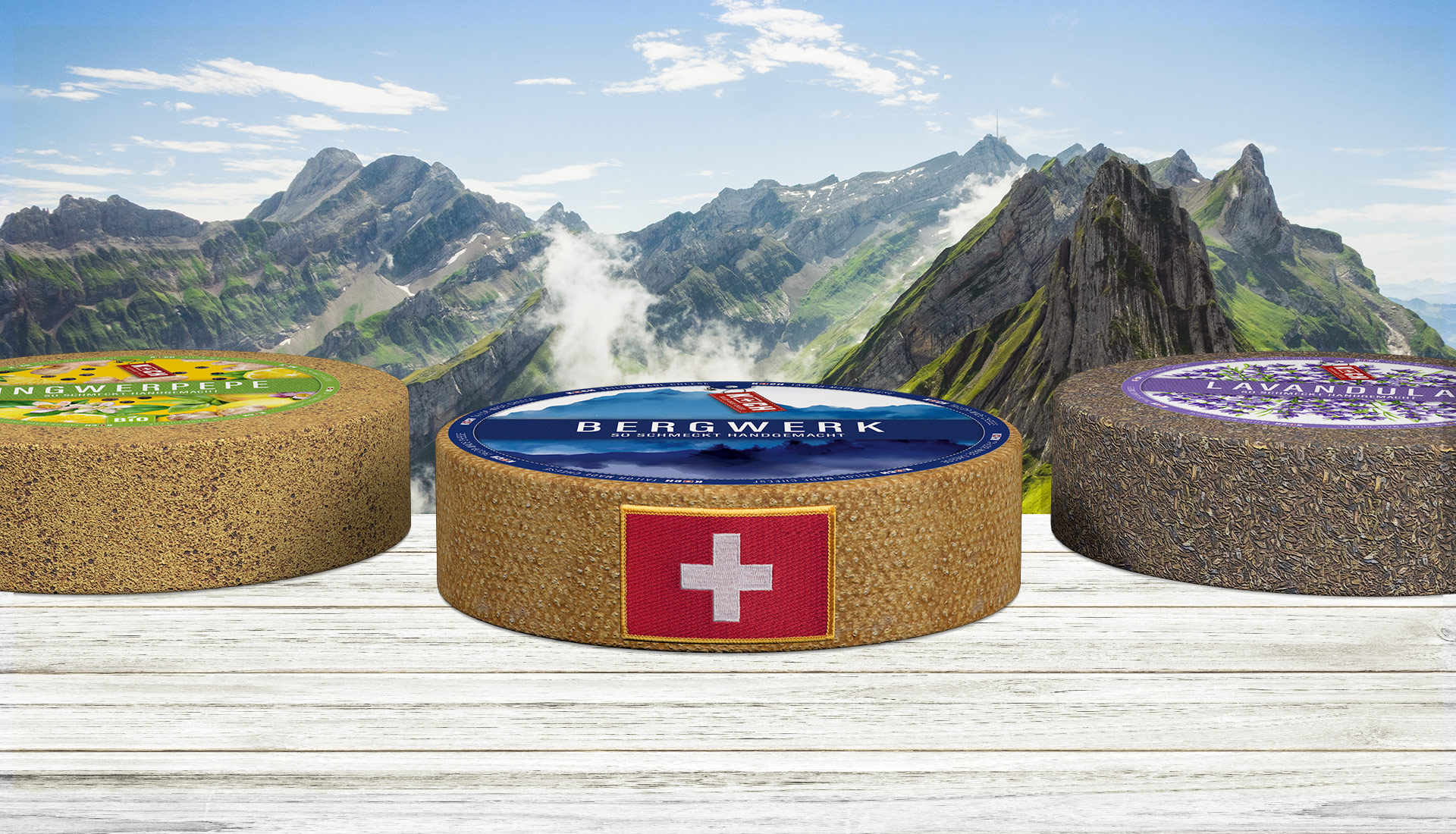 Koch Cheese drei Kaeselaibe mit Schweizer Badge vor Alpenhintergrund
